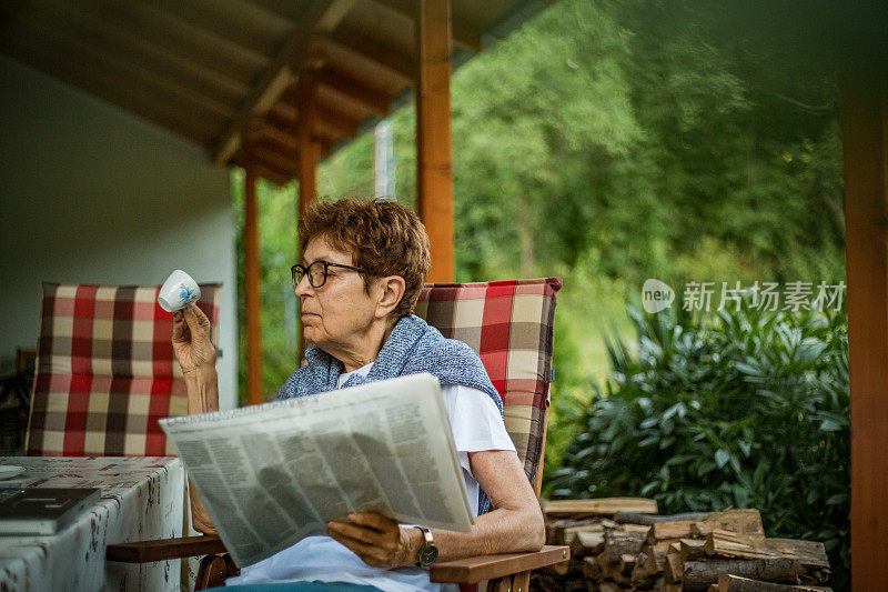 An older woman reads a novelty in the garden of her house - Rest in the afternoon in the yard of the house